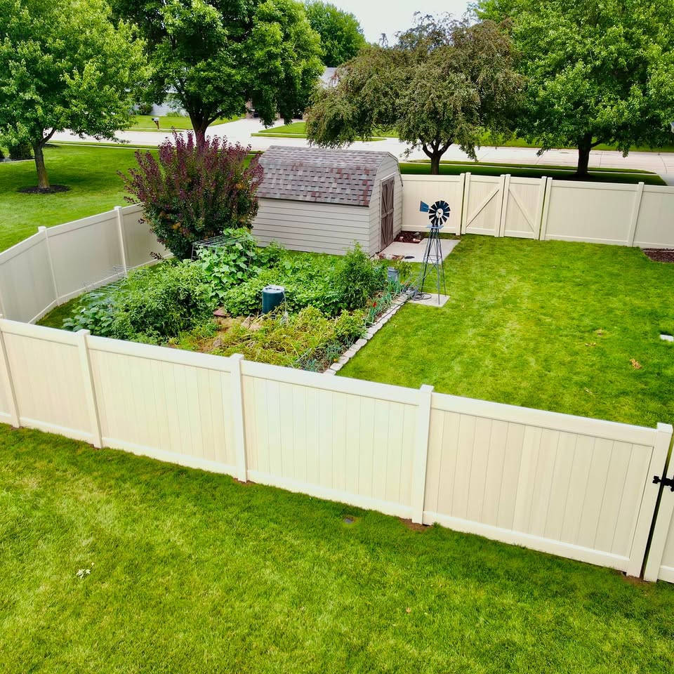 Cream vinyl privacy fence around a backyard garden installed in Southeast Nebraska by KD Fencing